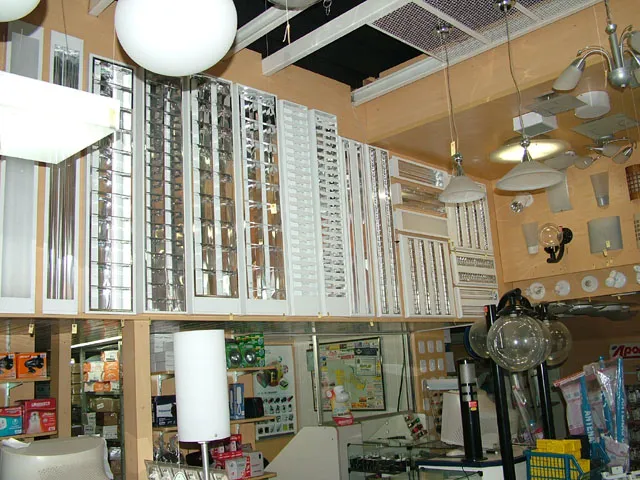 Salão da loja com a parede coberta de luminárias até o teto, globos brancos e um lustre pendurados, arandelas e prateleiras de produtos embaixo